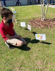 A young boy kneeling in the grass to admire student artwork. 