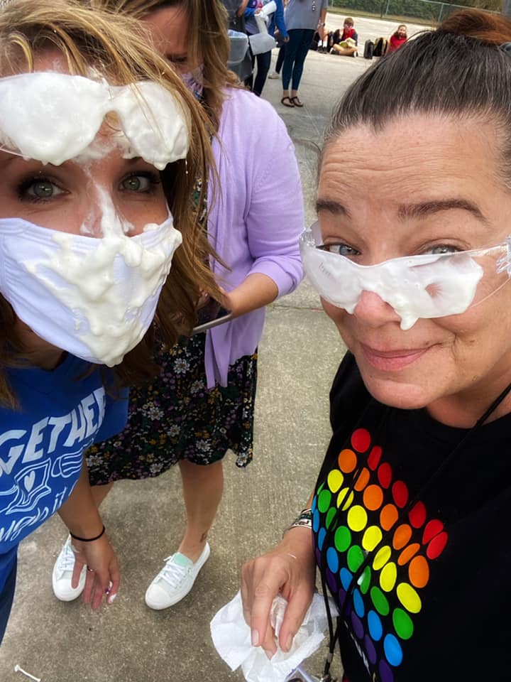 Two female teachers wearing safety goggles and covered in whipped cream from being pied in the face!
